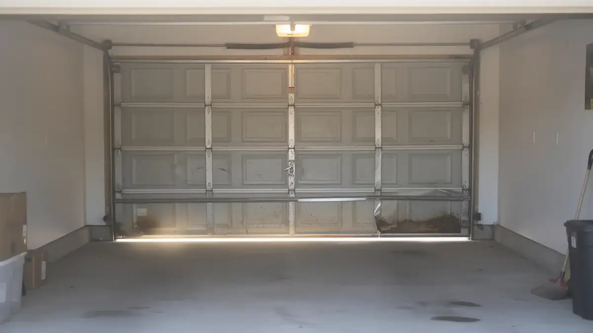 The damaged garage door is partially open, revealing a dirty bottom panel.